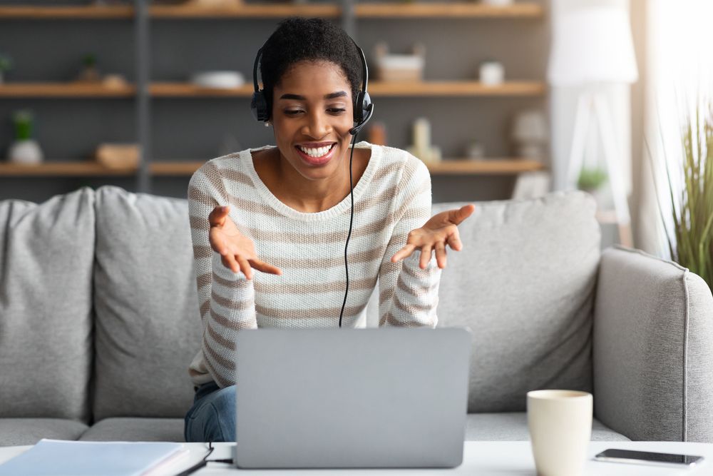smiling black woman in headset having web conference on laptop at home